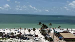 Hotel aan het strand met een parkeerplaats, strandparasols en palmbomen.