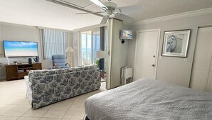 Een hotelkamer met een bed, een slaapbank, een televisie en een balkon met gordijnen.