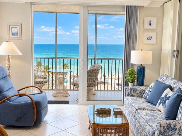 A room with a view of the ocean, a blue sofa, a wicker chair, and a glass coffee table.