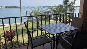 Un balcon avec une table et des chaises, donnant sur une étendue d’eau bordée de palmiers et d’une côte lointaine.