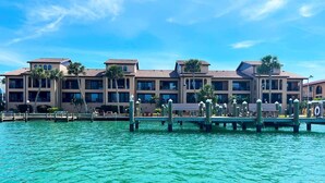 Un hôtel situé au bord de l’eau, doté de nombreux balcons, d’une jetée avec des chaises longues et offrant une vue sur un ciel bleu azur.