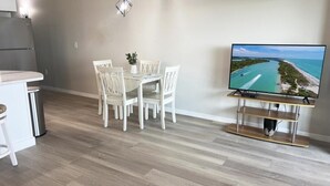 Une cuisine moderne dotée d’un réfrigérateur encastré, d’un coin repas avec des chaises blanches et d’un téléviseur à écran plat diffusant une vue sur la côte.