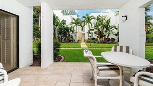 A patio with a white table and chairs, a view of a well-maintained lawn, and a building in the background.