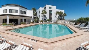 A modern hotel with a swimming pool, lounge chairs, and palm trees.