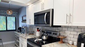 A modern kitchen with white cabinets, a stainless steel microwave, a coffee maker, and a kettle on the counter. - Tamarind 3BR Loft – Beach Vibes & Bay Views (Englewood)