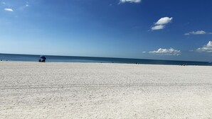 En bred sandstrand med en klarblå himmel och ett lugnt hav.