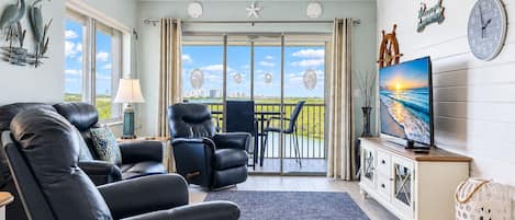 Un salon avec vue sur la mer, un téléviseur et une horloge au mur.
