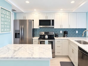 A modern kitchen with white cabinets, a stainless steel refrigerator, an LG microwave, a gas stove, and a coffee maker. - 2BR - Dolphins & Bay Views Just Steps to Beach (Bonita Springs)