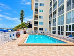 A rooftop swimming pool with lounge chairs and a view of a building with multiple balconies. - 2BR - Dolphins & Bay Views Just Steps to Beach (Bonita Springs)