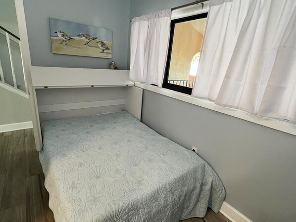 A small, single-bed room with a window, a painting of birds, and a curtain.