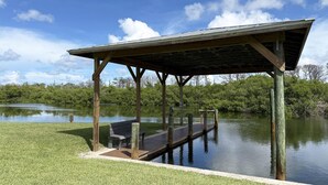 A wooden pavilion with a roof over a dock extending into a calm lake, surrounded by lush greenery. - 2BR on Oyster Creek – Boat Dock & Beach (Englewood)