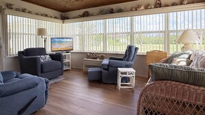 A spacious living room with a wooden ceiling, large windows with blinds, a television, and various seating options including a sofa, armchair, and ottoman. - 2BR on Oyster Creek – Boat Dock & Beach (Englewood)