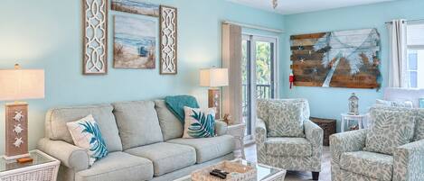 A living room with a light blue wall, a ceiling fan, a sofa, two armchairs, a coffee table, and decorative wall art.