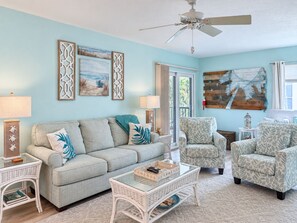 A living room with a light blue wall, a ceiling fan, a sofa, two armchairs, a coffee table, and decorative wall art.