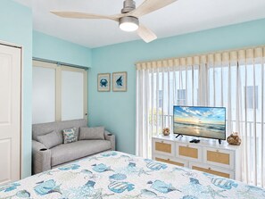 A bedroom with a bed, a sofa, a television on a dresser, and a ceiling fan.