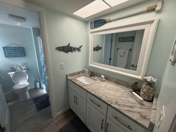Un baño con lavamanos de mármol, un espejo grande y una decoración de peces en la pared.