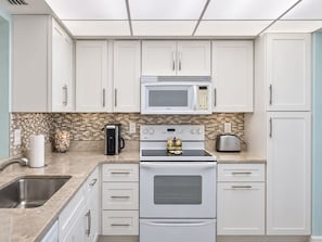 A kitchen with white cabinets, a microwave, a coffee maker, a toaster, and a stove.