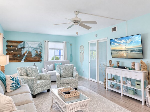 A living room with a ceiling fan, a television, and a view of the outdoors through a window.