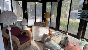 A sunlit room with wicker furniture, a white cabinet, and a view of greenery outside.