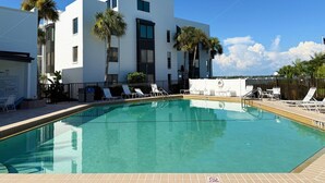 A modern building with a swimming pool, white walls, and palm trees.
