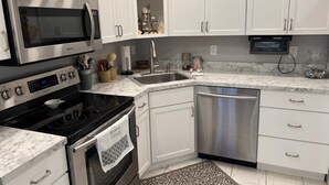 A modern kitchen with white cabinets, stainless steel appliances, a microwave, stove, dishwasher, and a marble countertop.