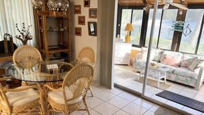 A spacious room with a glass door leading to an outdoor area, wicker furniture, a glass table, and a wooden cabinet with decorative items.