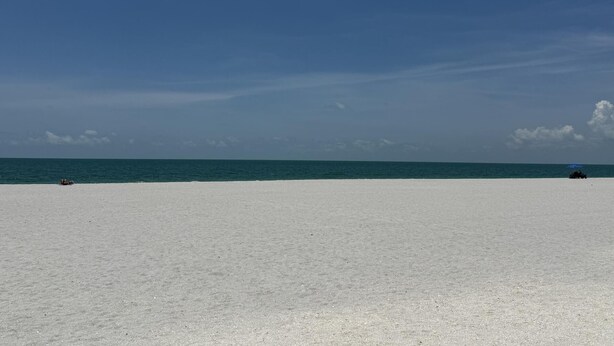 Una extensa playa de arena con cielo azul despejado y mar tranquilo.