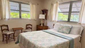 Un dormitorio con cama, dos sillas, una mesita de noche, una lámpara y ventanas con cortinas.