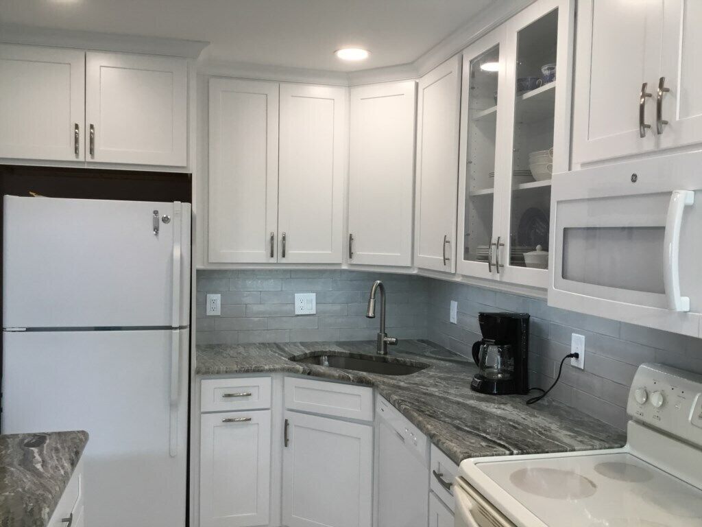 A kitchen with white cabinets, a granite countertop, a sink, a coffee maker, and a stove.