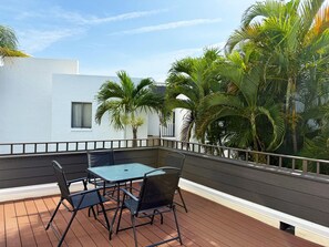 Eine Terrasse mit Tisch und Stühlen, umgeben von einem Geländer und Palmen.