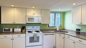 A compact kitchen with white cabinetry, a microwave, a stove, and a toaster. - Bayside 2BR Condo at Tamarind - Private Sun Deck (Englewood)