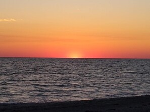 A sunset over a calm sea with a beach in the foreground.