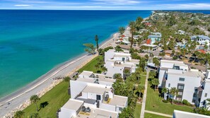 An aerial view of a coastal residential area with modern houses, a beach, and clear blue waters. - Bayside 2BR Condo at Tamarind - Private Sun Deck (Englewood)