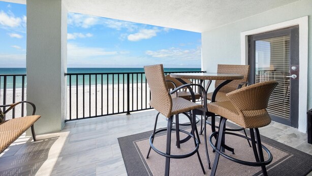 A balcony with wicker chairs and a table, overlooking a beach.