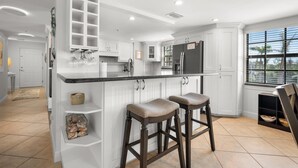 A modern kitchen with white cabinetry, a black countertop, and two bar stools.