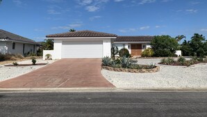 A residential property with a central garage, a driveway leading to the garage, and a landscaped garden with various plants and a palm tree. - Charming 2BR Pool Home Near Manasota Key (Englewood)