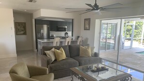 A modern living room with a glass coffee table, a sofa, and a chair. - Charming 2BR Pool Home Near Manasota Key (Englewood)