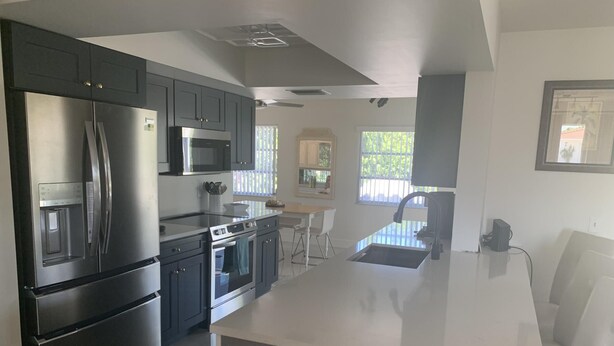 A modern kitchen with stainless steel appliances, a central island, and a dining area with a view. - Charming 2BR Pool Home Near Manasota Key (Englewood)