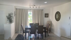 A dining area with a table and chairs, a sofa, a potted plant, and a wall-mounted mirror. - Charming 2BR Pool Home Near Manasota Key (Englewood)