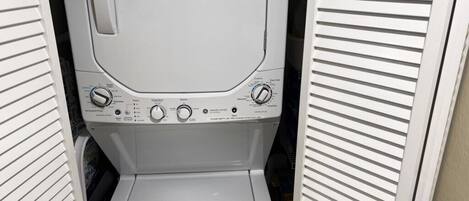 A compact, white washing machine with a control panel featuring multiple settings and a small step for loading.