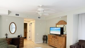 Amplia sala de estar con una cama grande, un televisor, un mueble de madera y un ventilador de techo.