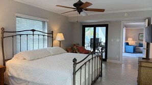 Une chambre avec un lit, un ventilateur de plafond, une fenêtre avec des stores et une vue sur un patio extérieur.