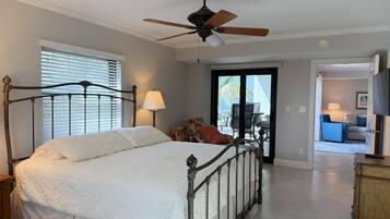 A bedroom with a bed, a ceiling fan, a window with blinds, and a view of an outdoor patio area.