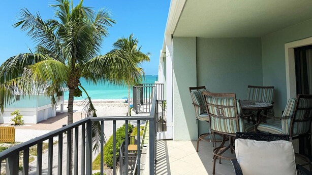 Un balcon avec vue sur la plage et l’océan, des meubles en osier et une balustrade.