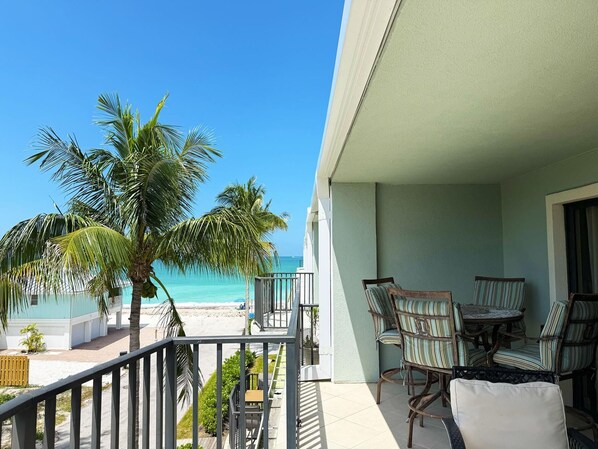 A balcony with a view of the beach and ocean, wicker furniture, and a railing.