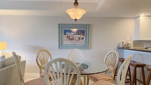 Un coin repas avec une table ronde en verre entourée de six chaises à rayures, un lustre et un tableau encadré accroché au mur.