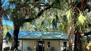A single-story building with a green roof, surrounded by trees and a gravel driveway. - Charming 2-bedroom cottage with full kitchen and WiFi in Pensacola. Sleeps 4. (Pensacola)