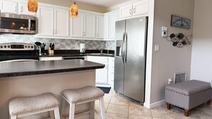 A modern kitchen with white cabinets, stainless steel appliances, a marble countertop, and pendant lighting.