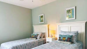 A bedroom with two single beds, each with a matching headboard and footboard. There are two bedside tables with lamps, and the walls are painted in a light teal color.