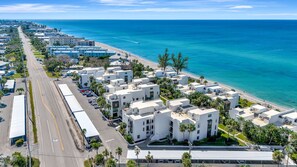 Eine Vogelperspektive zeigt ein Küstenhotel mit mehreren weißen Gebäuden, einer Straße und einem Strand.